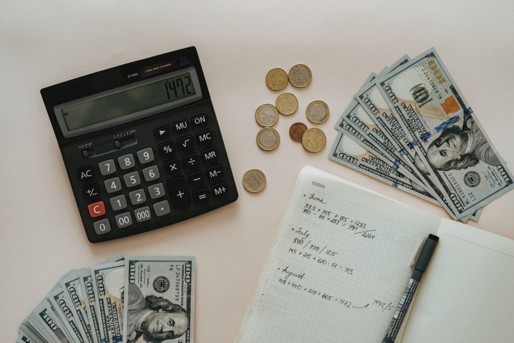 desktop with notes, a calculator and two stacks of 100 dollar bills