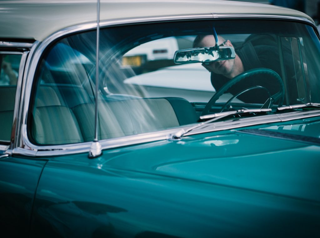 classic car windshield with person looking through drivers side window at the rear-view mirror