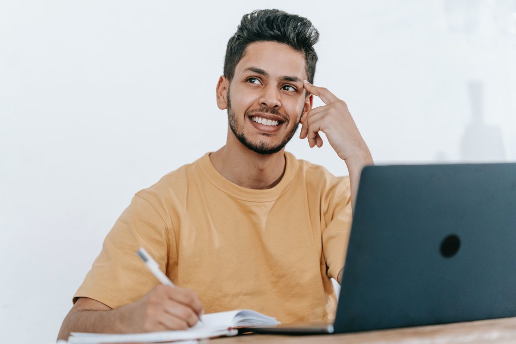man with notebook and pen at a laptop looking up
